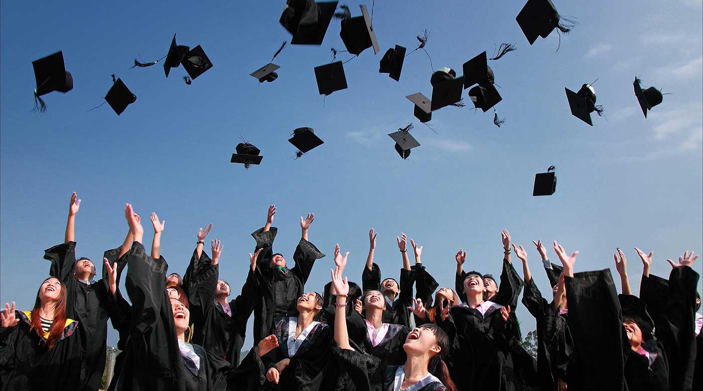 A group of graduating students wearing gowns and throwing their caps in the air