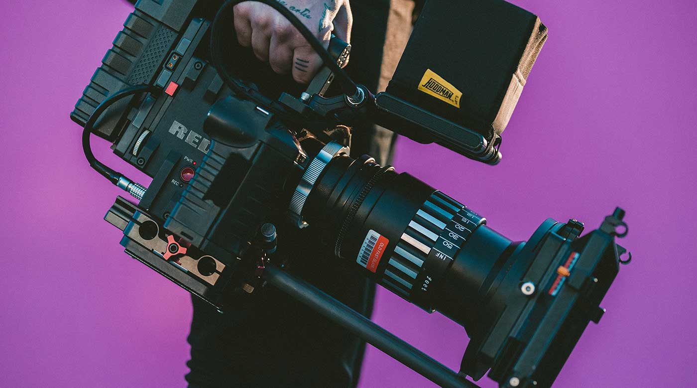 Cameraman holding a professional video camera against a purple backdrop