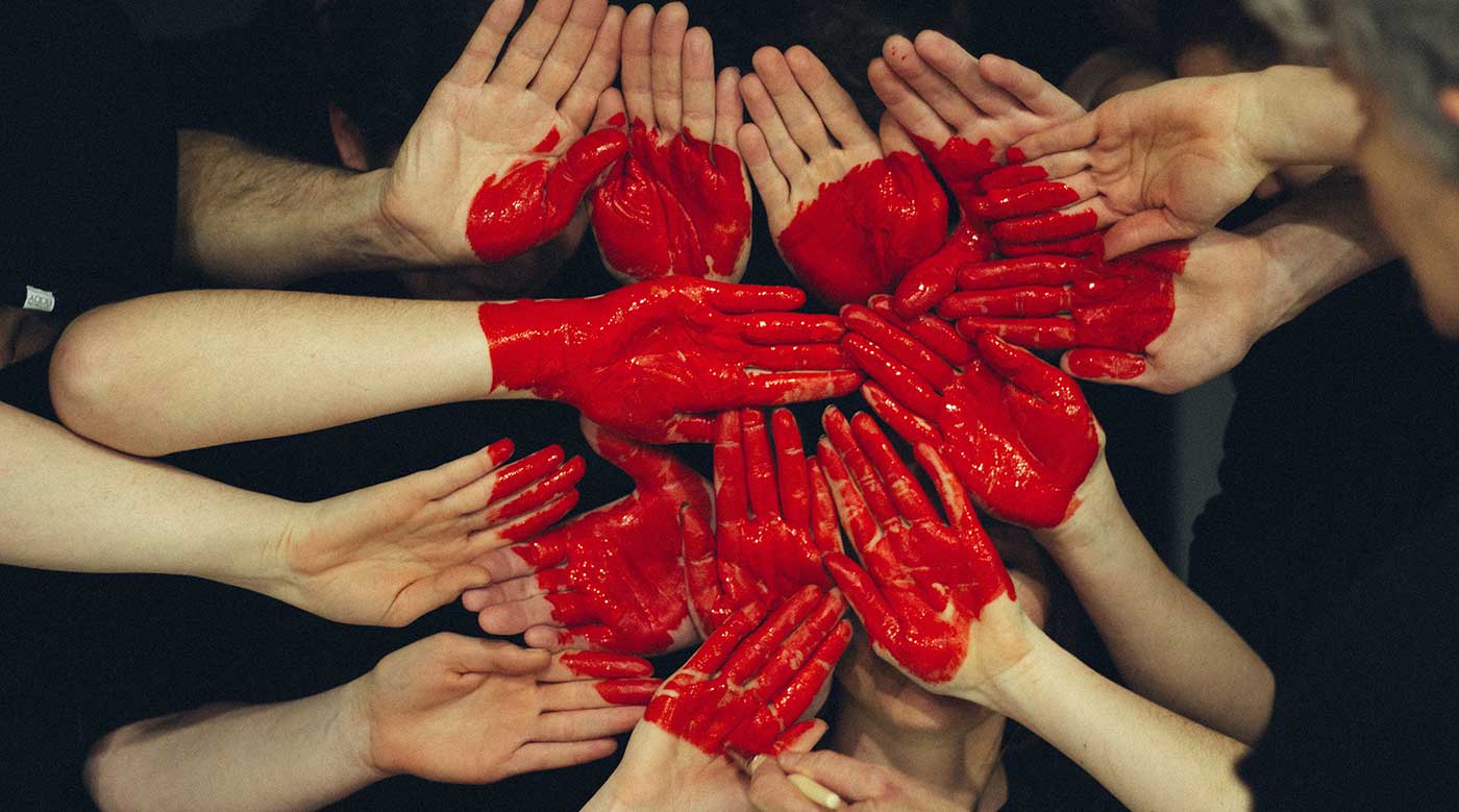 Group of people putting their hands together making the shape of a heart with red paint
