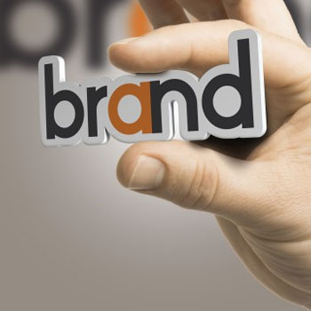 Person holding a cut-out of a logo design which says 'brand'